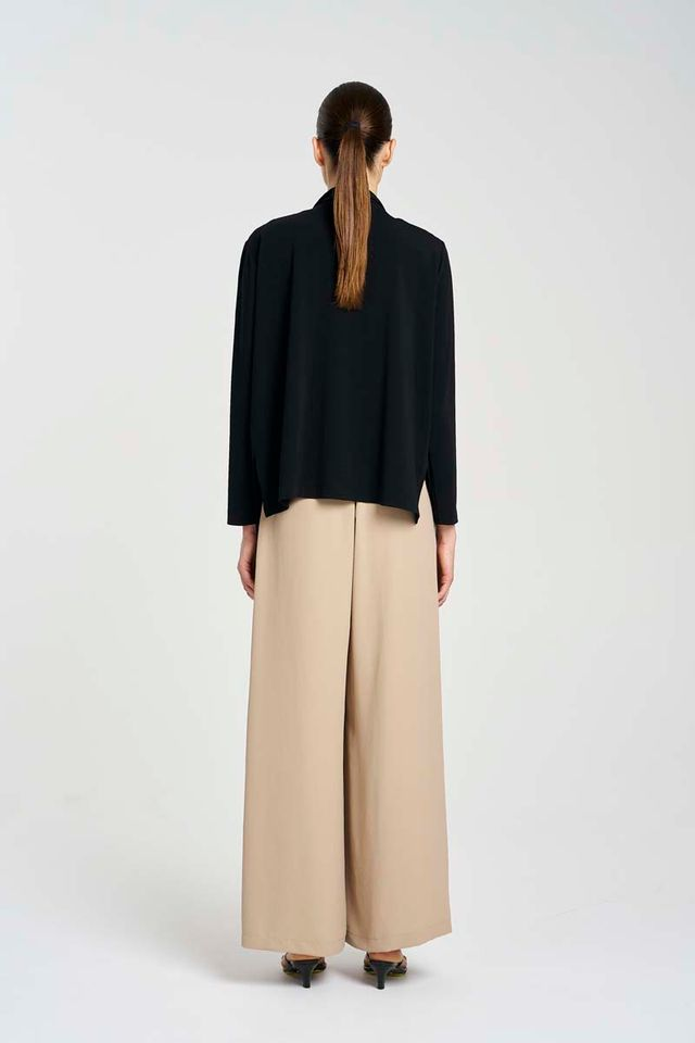 Person wearing a black top and beige pants on a white background