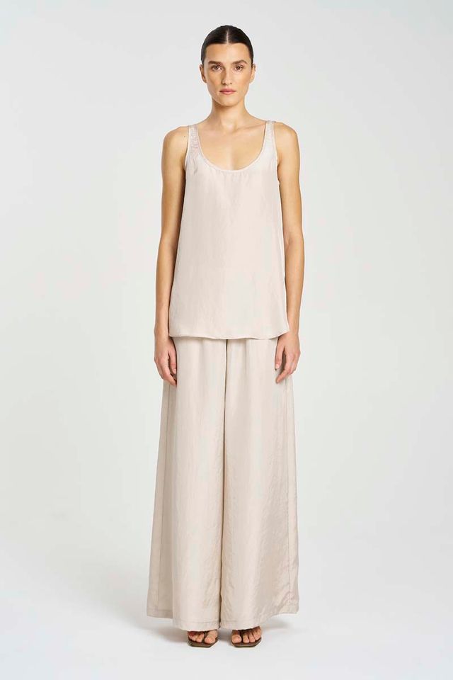 Woman wearing a beige sleeveless top and wide-leg pants on a white background