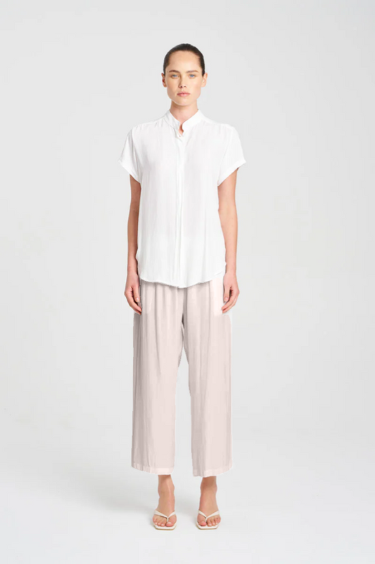 Person wearing a white shirt and light-colored pants on a plain background