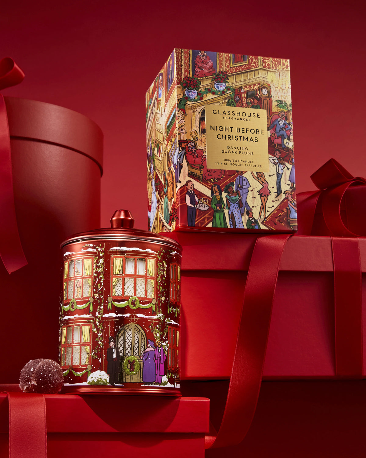 Glasshouse Fragrances Night Before Christmas 380g Candle beside its illustrated box among red gift boxes